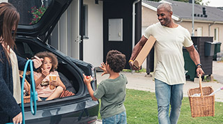 Brother and sister talking while father carrying picnic basket in front yard